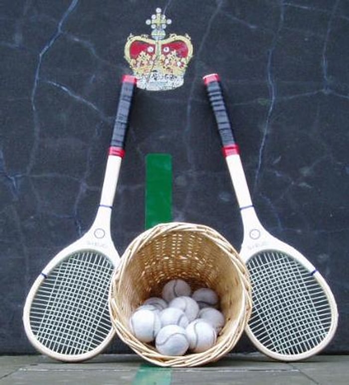 Raquetes de madeira de real tennis com cabeça assimétrica, e uma cesta de bolas